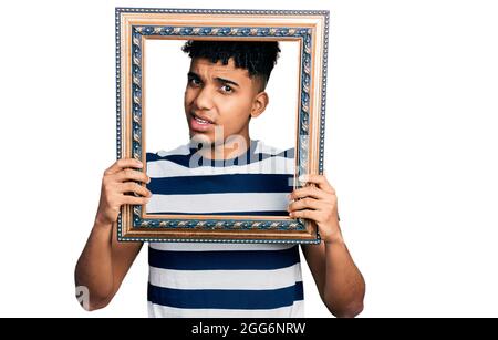 Il giovane afroamericano che tiene la cornice vuota senza indizio e confuso espressione. Concetto di dubbio. Foto Stock