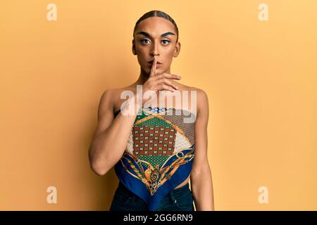 L'uomo ispanico che indossa make up e lunghi capelli che indossano i woman in cima chiedendo di essere tranquillo con il dito sulle labbra. Silenzio e segreto concetto. Foto Stock