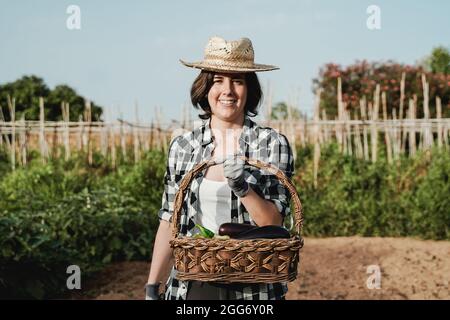 Donna contadina felice che lavora in campagna fattoria tenendo un cesto di legno con verdure fresche biologiche durante il tempo di raccolta - Focus sulla faccia Foto Stock