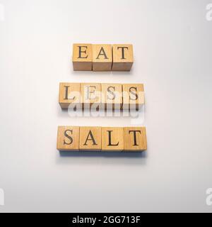 La parola mangiare meno sale è stato creato da cubetti di legno. Concetto di salute e vita, primo piano Foto Stock