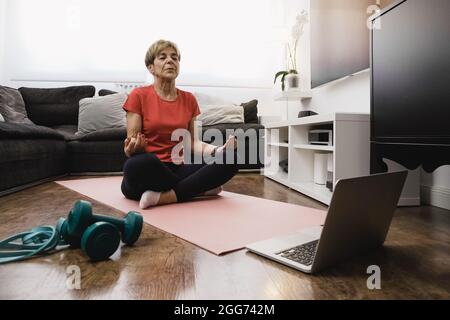 Donna anziana che fa la lezione di yoga in linea nel paese - stile di vita sano e mentalità concetto anziano - fuoco sul volto Foto Stock