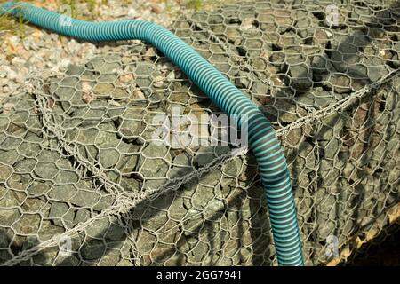 Tubo a grondetto per l'approvvigionamento idrico. Un tubo flessibile si trova sul marciapiede. Pietre in una griglia. Foto Stock