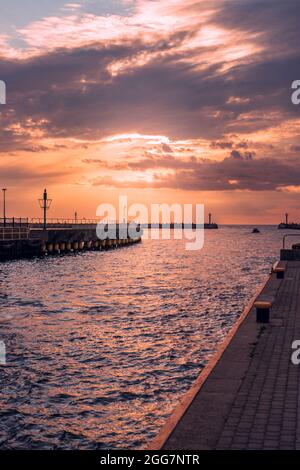 Lunga e concreta frangiflutti presso l'ingresso del porto di Darłówko, in Polonia illuminata dal sole. Sagome dei due piccoli fari alla fine Foto Stock