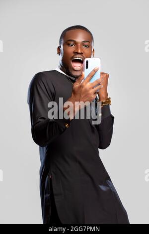 giovane uomo nero che si sente eccitato e si rallegra mentre tiene un telefono, Foto Stock