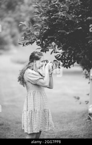 Una foto in scala di grigi di una fotografo caucasica femminile che scatta foto della natura in un parco Foto Stock