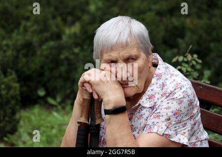 Donna anziana seduta con bastoni da passeggio su una panca in un parco. Stile di vita sano in vecchiaia, vita in pensione Foto Stock