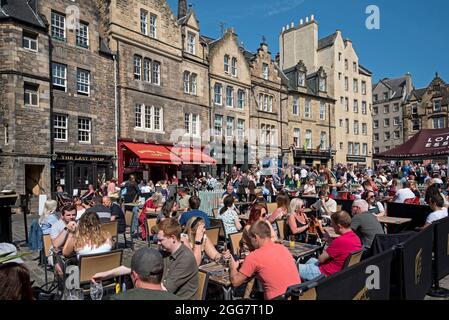 I turisti e la gente del posto si rilassano all'esterno e si godono il sole nel Grassmarket, Edimburgo, Scozia, Regno Unito. Agosto 2021. Foto Stock