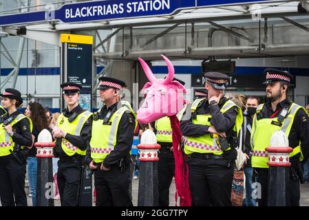 Linea di ufficiali di polizia alla marcia nazionale per i diritti degli animali, organizzata dalla ribellione animale e dalla ribellione di estinzione e un protestore con la mucca rosa papier-mâché, Londra, Inghilterra, Regno Unito. Agosto 28 2021 Foto Stock