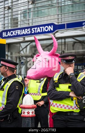 Linea di ufficiali di polizia alla marcia nazionale per i diritti degli animali, organizzata dalla ribellione animale e dalla ribellione di estinzione e un protestore con la mucca rosa papier-mâché, Londra, Inghilterra, Regno Unito. Agosto 28 2021 Foto Stock