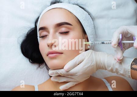 Sollevamento del sorriso e aumento del labbro. Medico estetista mani che fanno la procedura di bellezza al viso femminile con siringa. Bocca della giovane donna contornata con Foto Stock