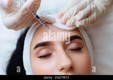 Il dottore cosmetologo rende il ringiovanimento di iniezioni per il viso la procedura di serraggio e levigatura di rughe sulla pelle del viso di una bella Foto Stock