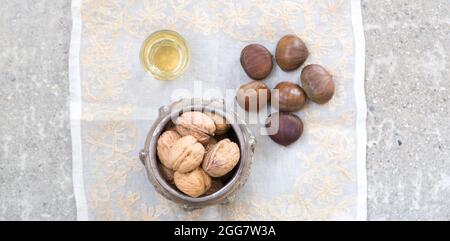 Noci, castagne e un bicchiere di liquore dorato su una superficie di cemento Foto Stock