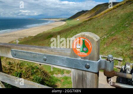 Splendida Rhossili Bay con Dog Poo cartello di avvertimento in evidenza su UN cancello in primo piano Foto Stock