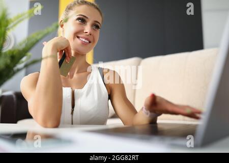 Donna bionda seduta da computer portatile con carta di credito Foto Stock