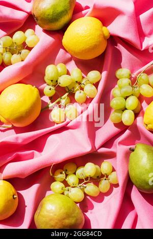 Vista dall'alto di limoni, pere e uva su un panno da tavola rosa Foto Stock