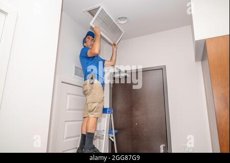 Il tecnico HVAC ispeziona un filtro dell'aria in una bocchetta di ritorno a soffitto Foto Stock