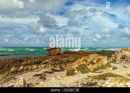 Aspra costa rocciosa con naufragio arrugginito di Meisho Maru No.38 a Capo Agulhas in Sud Africa che è il punto più meridionale del continente africano. Foto Stock