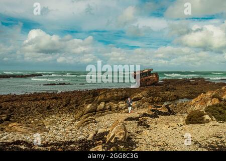 Aspra costa rocciosa con naufragio arrugginito di Meisho Maru No.38 a Capo Agulhas in Sud Africa che è il punto più meridionale del continente africano. Foto Stock