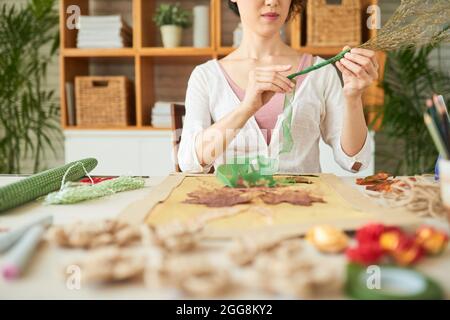 Immagine ritagliata di giovane donna che decora fiori selvatici secchi con nastro di nylon verde Foto Stock