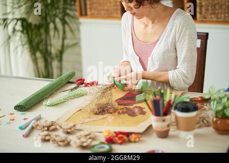 Giovane donna concentrata che lavora con fiori secchi e altri materiali botanici per creare un quadro completo Foto Stock