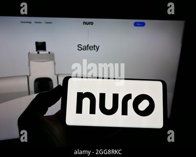 Persona che tiene uno smartphone con il logo della società di guida autonoma americana Nuro Inc. Sullo schermo di fronte al sito Web. Mettere a fuoco sul display del telefono. Foto Stock