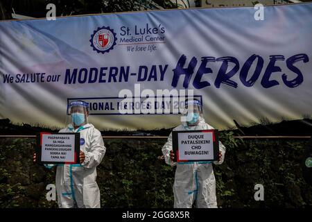 30 agosto 2021: Gli operatori sanitari che indossano tute protettive trasportano i segni mentre tengono una protesta per celebrare la Giornata Nazionale degli Eroi fuori dal St. Luke's Medical Center. Il gruppo ha invitato il governo a liberare fondi per le prestazioni e un'adeguata protezione per gli operatori sanitari che continuano a essere a rischio a causa dell'aumento dei casi COVID-19 nel paese. (Credit Image: © Basilio Sepe/ZUMA Press Wire) Foto Stock