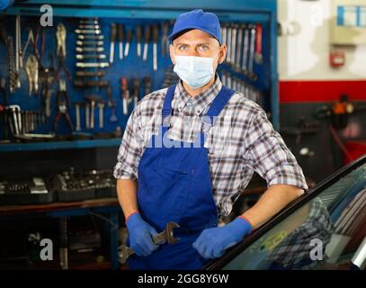 Uomo di lavoro in maschera protettiva in piedi vicino all'auto al servizio di riparazione auto Foto Stock