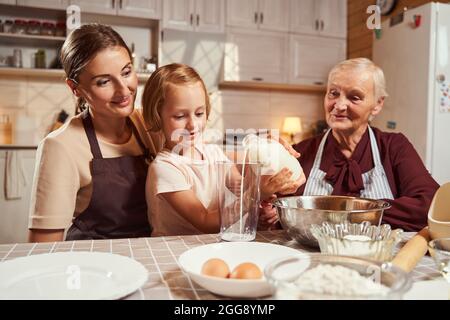 La famiglia eccitata guarda il loro bambino che versa il latte al vetro Foto Stock