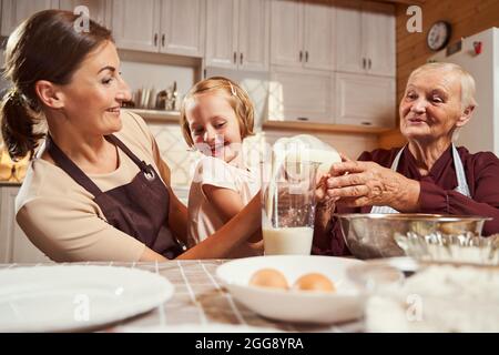 Granny aiuta il bambino a versare il latte alla tazza Foto Stock