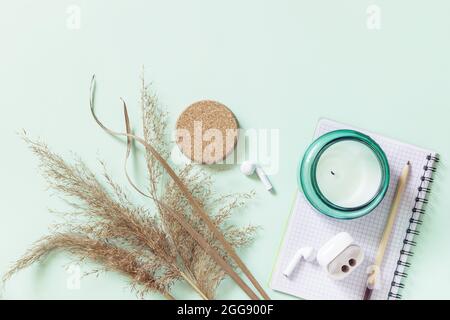 Flat Lay still life aroma candela, pampas erba, blocco note e matita su uno sfondo verde pastello. Mockup, foto con una tavolozza di colori neutri. Foto Stock