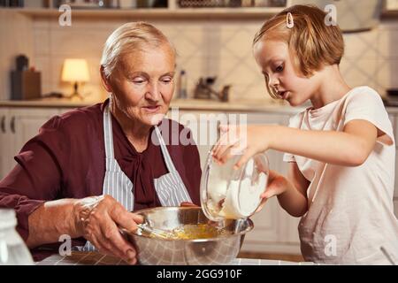 Ragazza che versa la farina in una ciotola profonda con la nonna Foto Stock