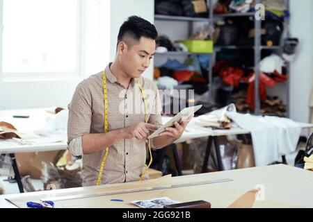 Un lavoratore di produzione di abbigliamento serio che verifica nuovi modelli sul computer tablet Foto Stock