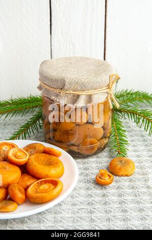 Funghi marinati aranciata o falso zafferano milkcap, Lactarius deterrimus in un vaso di vetro e funghi freschi raccolti sul piatto. Foto Stock