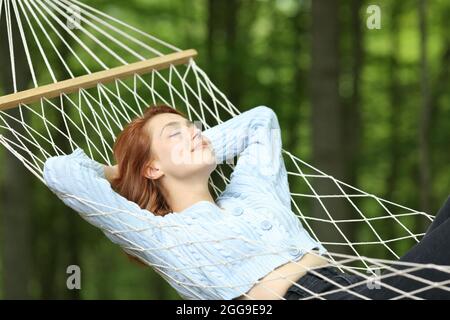 Donna rilassante sdraiata su amaca in corda in una foresta durante le vacanze estive Foto Stock