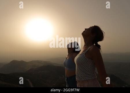 Vista laterale ritratto di due donne silhouette respirare aria fresca insieme al tramonto Foto Stock