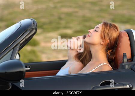 Ritratto della vista laterale di due donne che riposano respirando aria fresca in un'auto convertibile Foto Stock