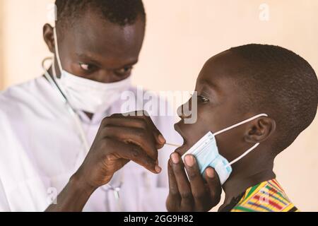In questa immagine, un medico sta prendendo un tampone della bocca da un ragazzo durante lo screening del covid-19 in un ospedale africano Foto Stock