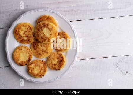 Diverse frittelle fragranti su un piatto di ceramica, primo piano, su un tavolo di legno bianco, vista dall'alto. Foto Stock