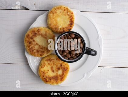 Diverse frittelle fragranti su un piatto di ceramica con una tazza di caffè, primo piano, su un tavolo di legno bianco, vista dall'alto. Foto Stock