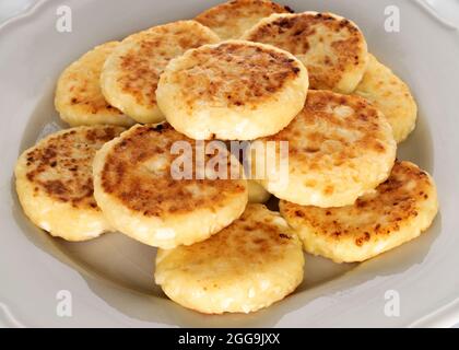 Alcune deliziose frittelle al formaggio cucinate al gusto, si trovano su un piatto leggero in ceramica. Lo sfondo è bianco. Foto Stock