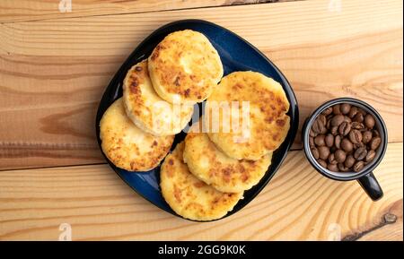 Diverse frittelle fragranti su un piatto di ceramica con una tazza di caffè, primo piano, su un tavolo di legno bianco, vista dall'alto. Foto Stock