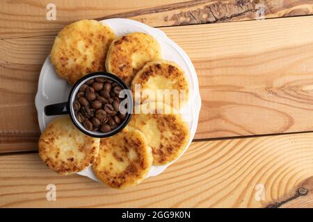 Diverse frittelle fragranti su un piatto di ceramica con una tazza di caffè, primo piano, su un tavolo di legno bianco, vista dall'alto. Foto Stock