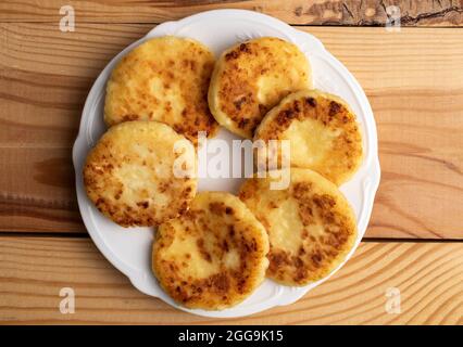 Diverse frittelle fragranti su un piatto di ceramica, primo piano, su un tavolo di legno bianco, vista dall'alto. Foto Stock