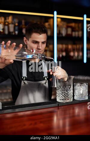 Barman in grembiule aggiunge l'ingrediente al vetro Foto Stock
