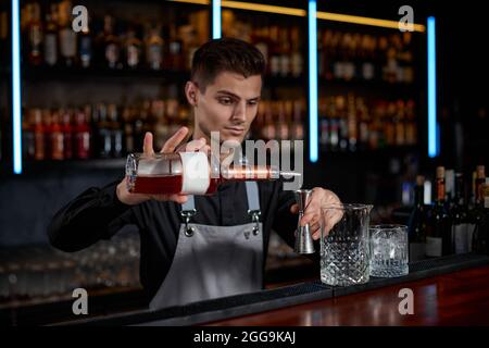 Barman in grembiule aggiunge l'ingrediente al vetro Foto Stock