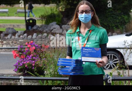 Una volontaria NHS femmina che consegna gratuitamente Covid-19 test di flusso laterale ai passanti da in una strada britannica su un Sabato Foto Stock