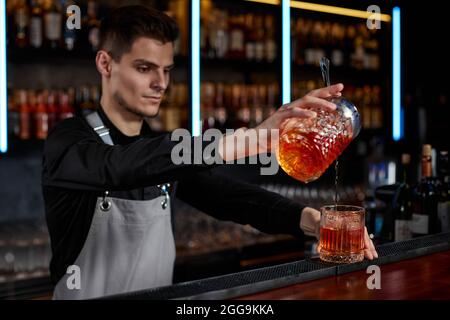 il barman in grembiule versa un cocktail vecchio stile in un bicchiere Foto Stock