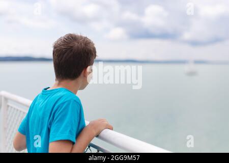 Piccolo ragazzo che guarda la barca a vela in lontananza sul mare, nave da crociera, viaggio, vista posteriore Foto Stock