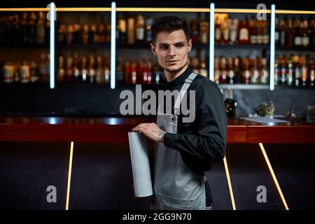 Bel barman in grembiule in piedi al bancone bar Foto Stock