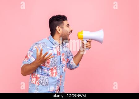Ritratto del profilo di uomo nervoso bearded in camicia di stile casual blu che parla ad alta voce urlando il megafono di tenuta, annunciando il messaggio importante. Per interni Foto Stock